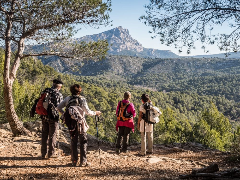 Quatre randonneurs avec sac-à-dos et bâtons de randonnée observent la montagne Sainte-Victoire.