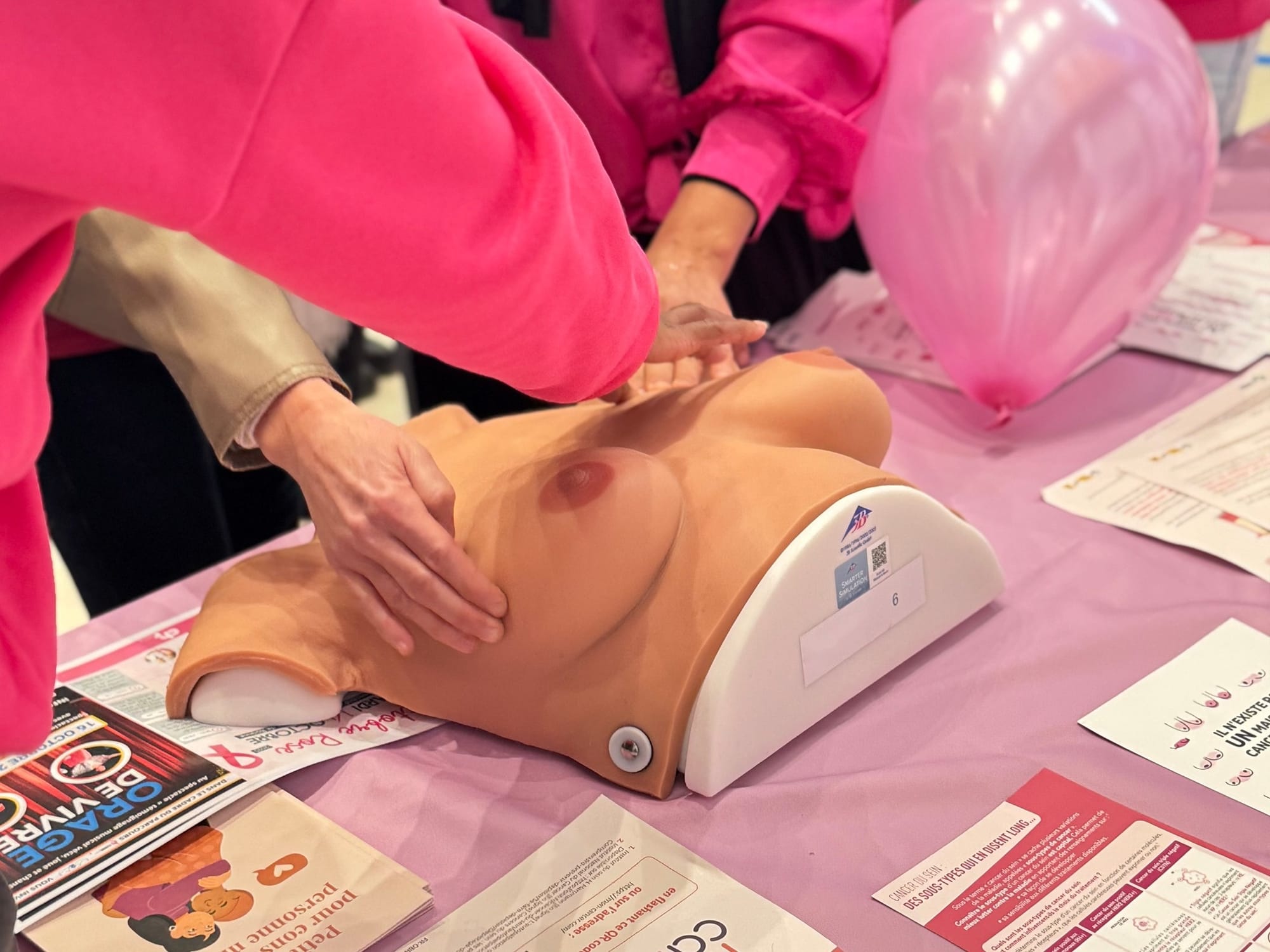 Une participante apprend les gestes de l’autopalpation sur un buste en silicone, sur un stand Octobre rose.