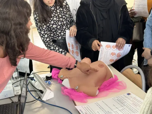 Animatrice d'un atelier d'autosurveillance mammaire montrant une zone d'un sein sur un buste d'autopalpation en silicone.